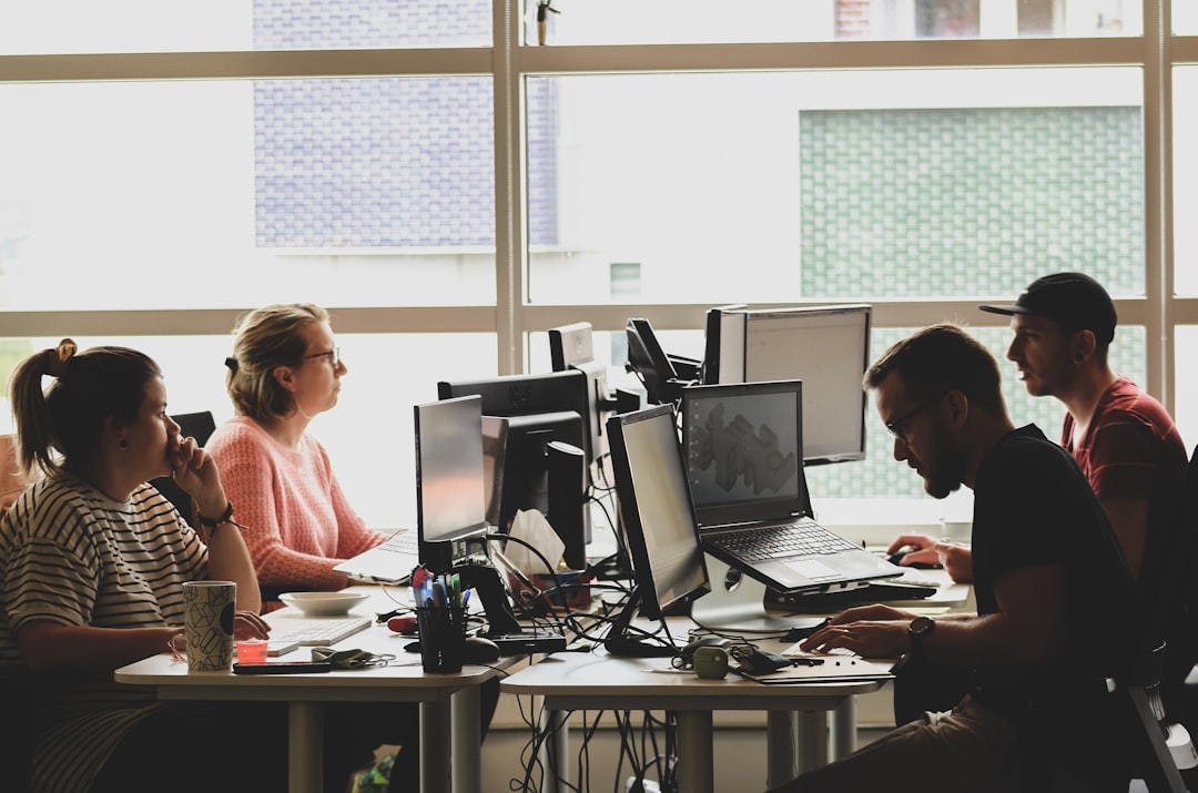 Four people working at computers in a sunlit office workspace