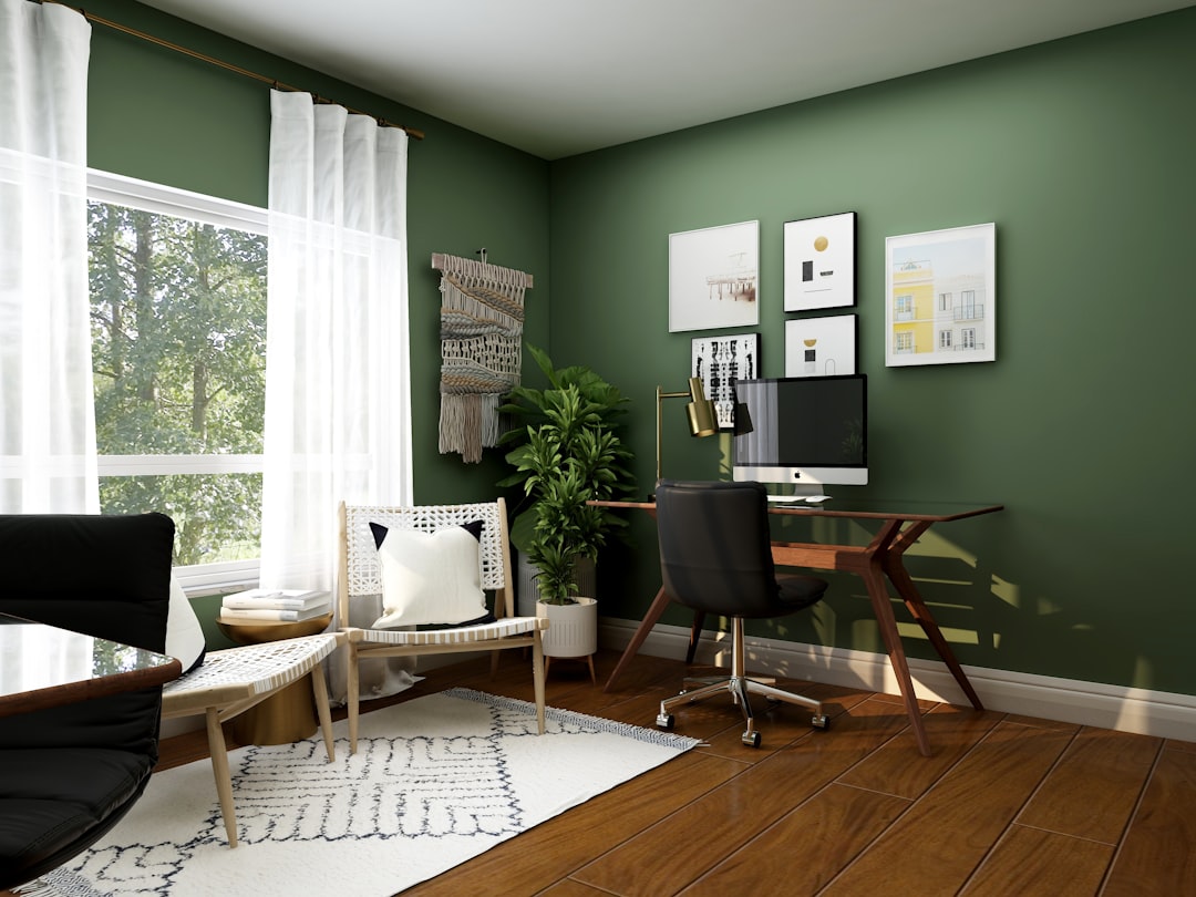 A home office with a wooden desk, black chair, and green walls