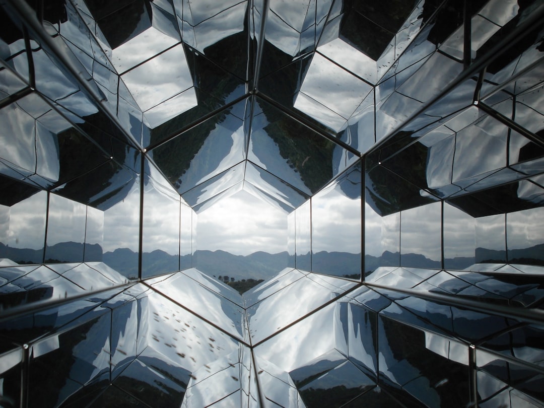 A hexagonal tunnel of mirrors reflecting a distant mountain range under a cloudy sky