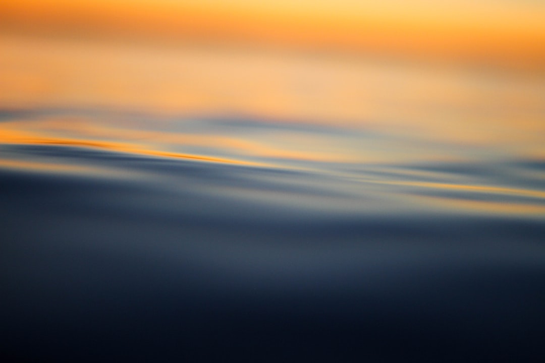 Soft ripples on dark water reflecting a warm orange glow from above